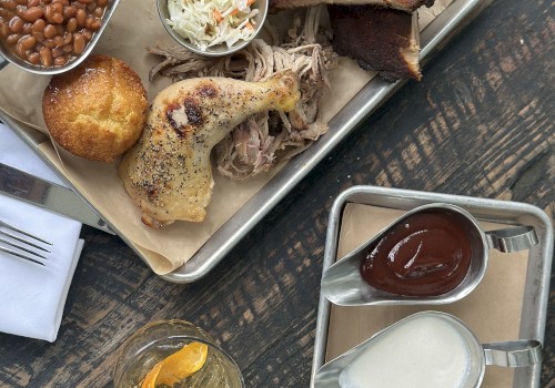 A tray with ribs, fries, coleslaw, chicken, beans, and cornbread; sauces and a drink are on the side.