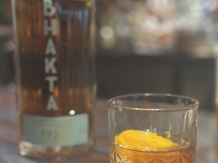 A glass with a drink and a citrus garnish is in the foreground, with a bottle labeled 