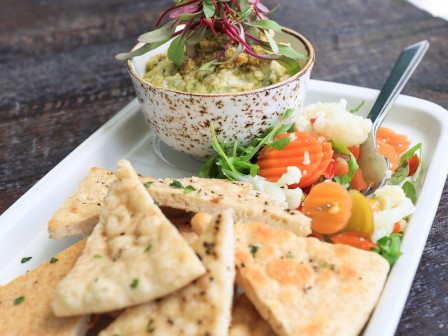 A plate with pita bread, a bowl of dip topped with greens, and pickled vegetables on the side.
