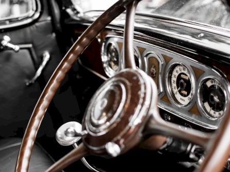 The image shows the interior of a vintage car, featuring a wooden steering wheel and a classic dashboard with analog gauges.