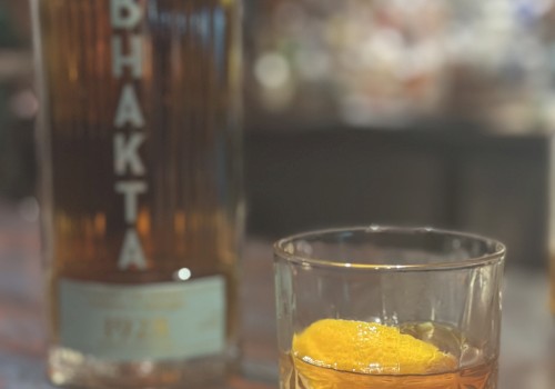 A bottle and a glass with a dark liquid and an orange twist on a napkin.