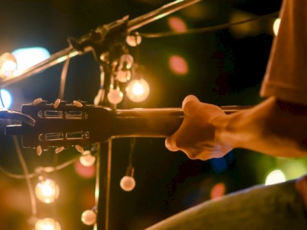 A guitarist playing under warm, glowing string lights, creating a cozy and intimate atmosphere with blurred background lights.
