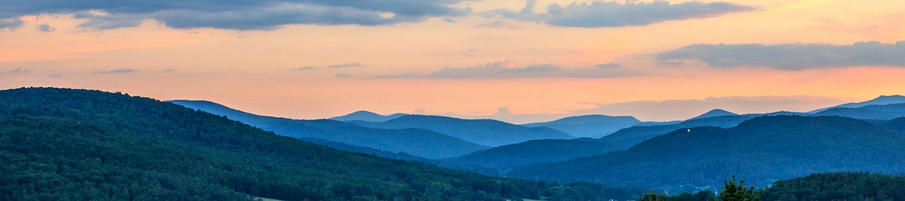 A picturesque landscape with rolling green hills, a pink and orange sunset, and a partly cloudy sky.