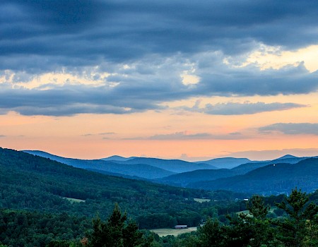 A picturesque landscape with rolling green hills, a pink and orange sunset, and a partly cloudy sky.