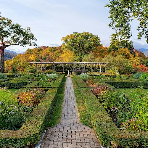 A beautifully landscaped garden with a brick pathway, surrounded by neatly trimmed hedges and colorful plants under a clear sky.