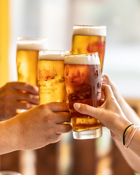 Four hands are toasting with glasses of beer, creating a cheerful and festive atmosphere.