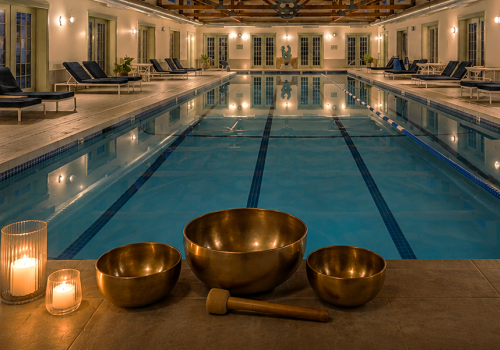An indoor pool with lounge chairs, ambient lighting, and singing bowls, creating a relaxing atmosphere for wellness and meditation.
