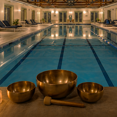 An indoor pool with lounge chairs, ambient lighting, and singing bowls, creating a relaxing atmosphere for wellness and meditation.