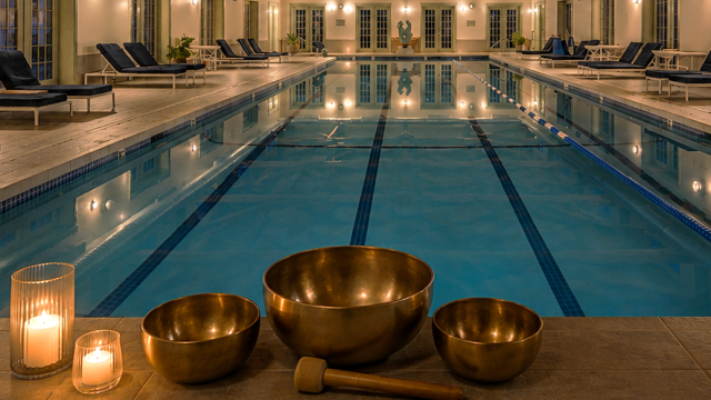 An indoor pool with lounge chairs, ambient lighting, and singing bowls, creating a relaxing atmosphere for wellness and meditation.