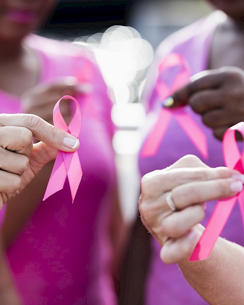 Close-up of people wearing pink shirts holding pink awareness ribbons, symbolizing unity and support for breast cancer awareness during a community event.