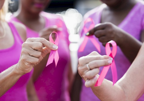 Close-up of people wearing pink shirts holding pink awareness ribbons, symbolizing unity and support for breast cancer awareness during a community event.