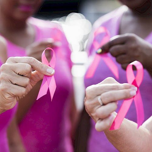 Close-up of people wearing pink shirts holding pink awareness ribbons, symbolizing unity and support for breast cancer awareness during a community event.