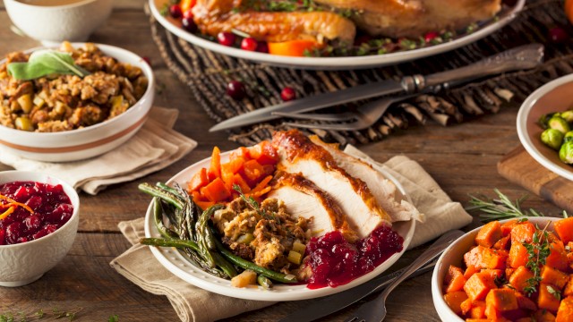 A Thanksgiving feast with turkey, stuffing, cranberry sauce, vegetables, and gravy arranged on a wooden table.