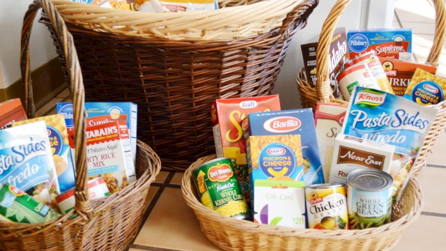 Wicker baskets filled with various packaged food items, pasta, canned goods, and a gift card are in the image.