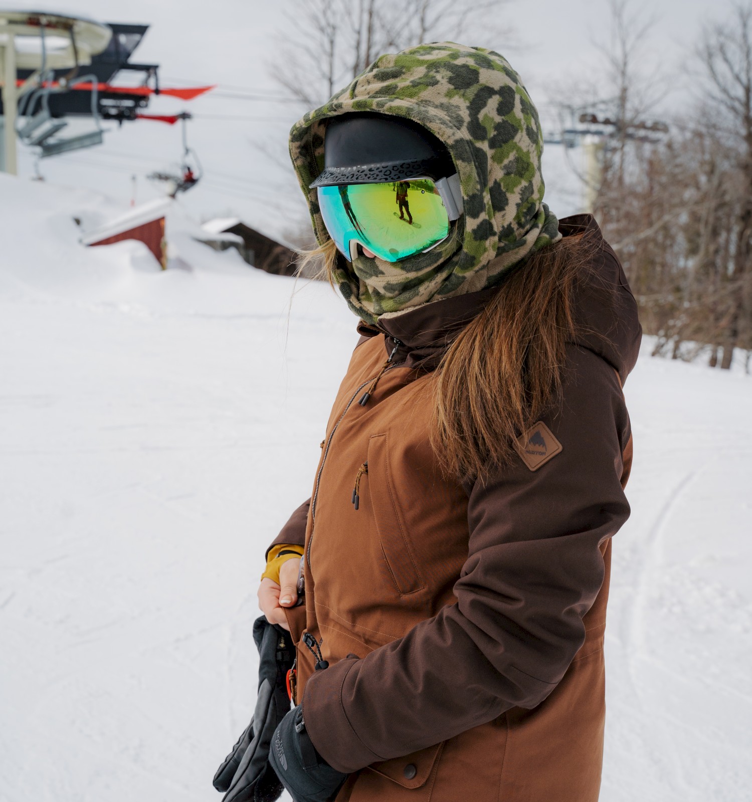 A person in winter gear is standing on a snowy slope, holding ski poles, with a ski lift in the background.