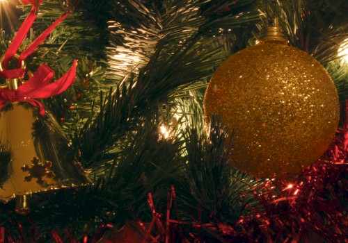 A festive Christmas tree close‑up with a glittery gold bauble, red ribbons, and twinkling lights among green needles, creating a cozy holiday glow.