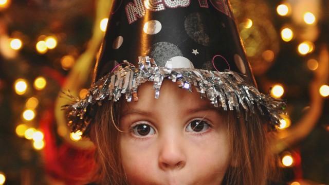 A child wearing a party hat and blowing a party horn at a festive celebration.