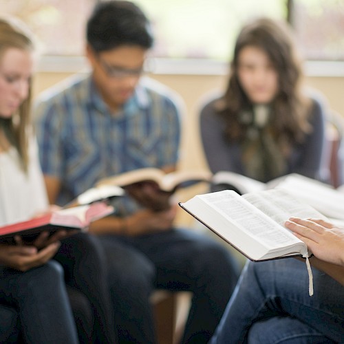 A group of students sits in a circle, reading books and sharing a discussion in a classroom setting.