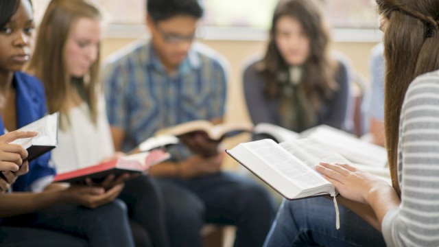 A group of students sits in a circle, reading books and sharing a discussion in a classroom setting.