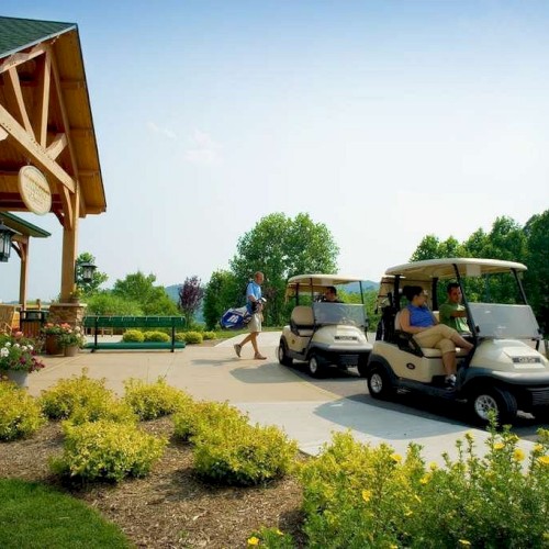 People near a clubhouse with parked golf carts, lush greenery, and bright flowers under a clear sky.