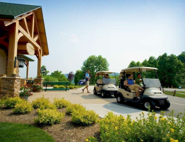People near a clubhouse with parked golf carts, lush greenery, and bright flowers under a clear sky.