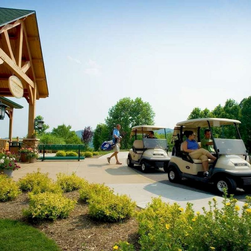 People near golf carts by a building, with lush greenery and landscaping in the background.
