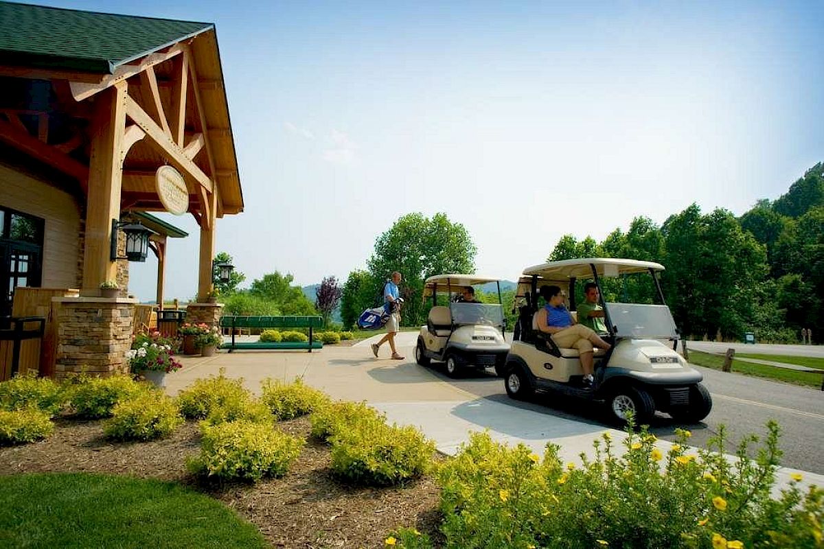 People with golf carts outside a wooden building surrounded by greenery and a clear sky.