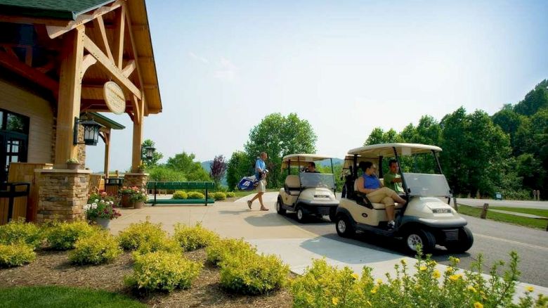 People with golf carts outside a wooden building surrounded by greenery and a clear sky.