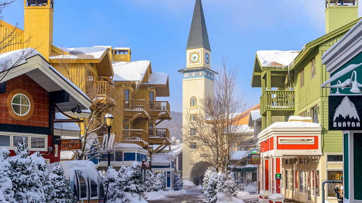 A snowy town street with colorful buildings, shops, and a tall clock tower in the center, cheerful winter scene, ending with a period.