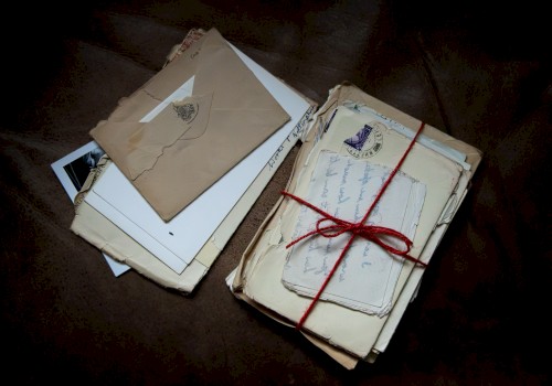 A bundle of old letters and envelopes tied with a red string, plus loose papers and a few photos scattered beside them.