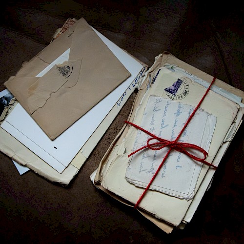A bundle of old letters and envelopes tied with a red string, plus loose papers and a few photos scattered beside them.
