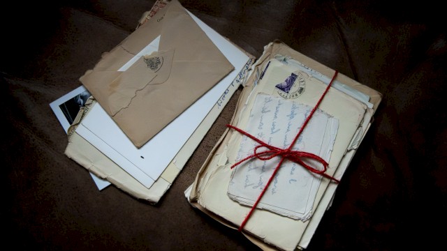 A bundle of old letters and envelopes tied with a red string, plus loose papers and a few photos scattered beside them.