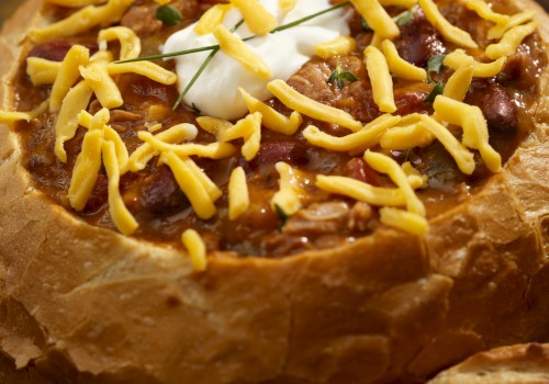 A bread bowl filled with chili, topped with shredded cheese and a dollop of sour cream, served in a rustic crusty loaf.